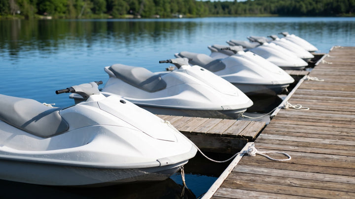 Row of uncovered white personal watercraft moored along a floating wooden dock on a calm lake