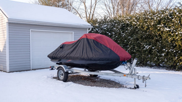 Jet ski on a trailer beside a snowy garage under a red and black AllGuard Weatherproof Shield cover