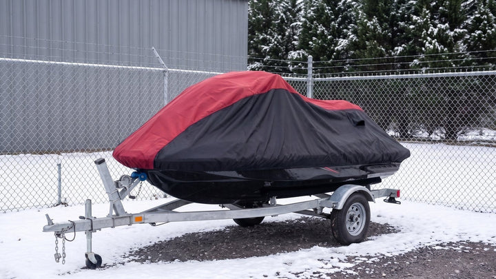 Jet ski on its trailer in a snowy fenced storage yard, under a red and black AllGuard Weatherproof Shield cover