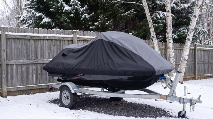 Jet ski on a trailer in a snowy backyard under a gray and black AllGuard Weatherproof Shield cover