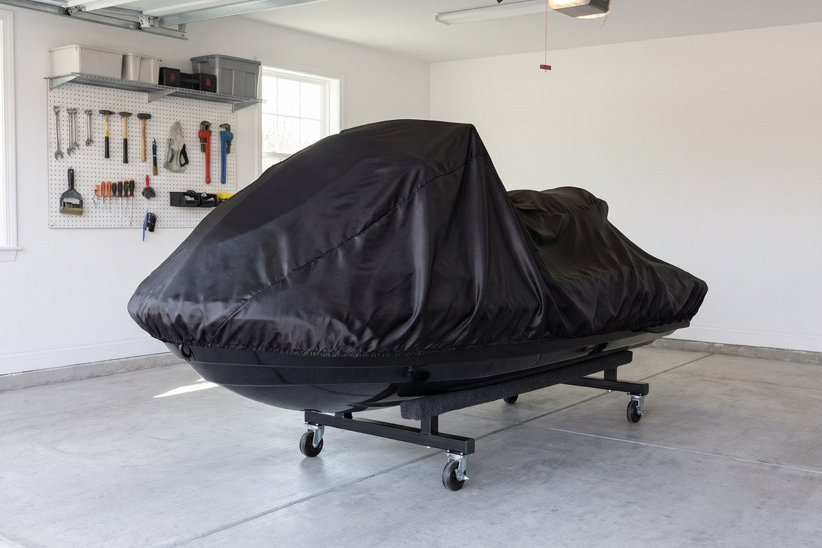 Jet ski under a black stretch cover on a wheeled dolly in a garage